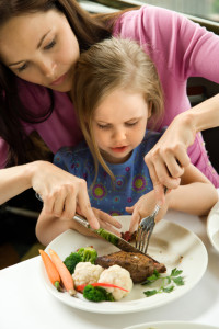 Mom helping daughter cut food.